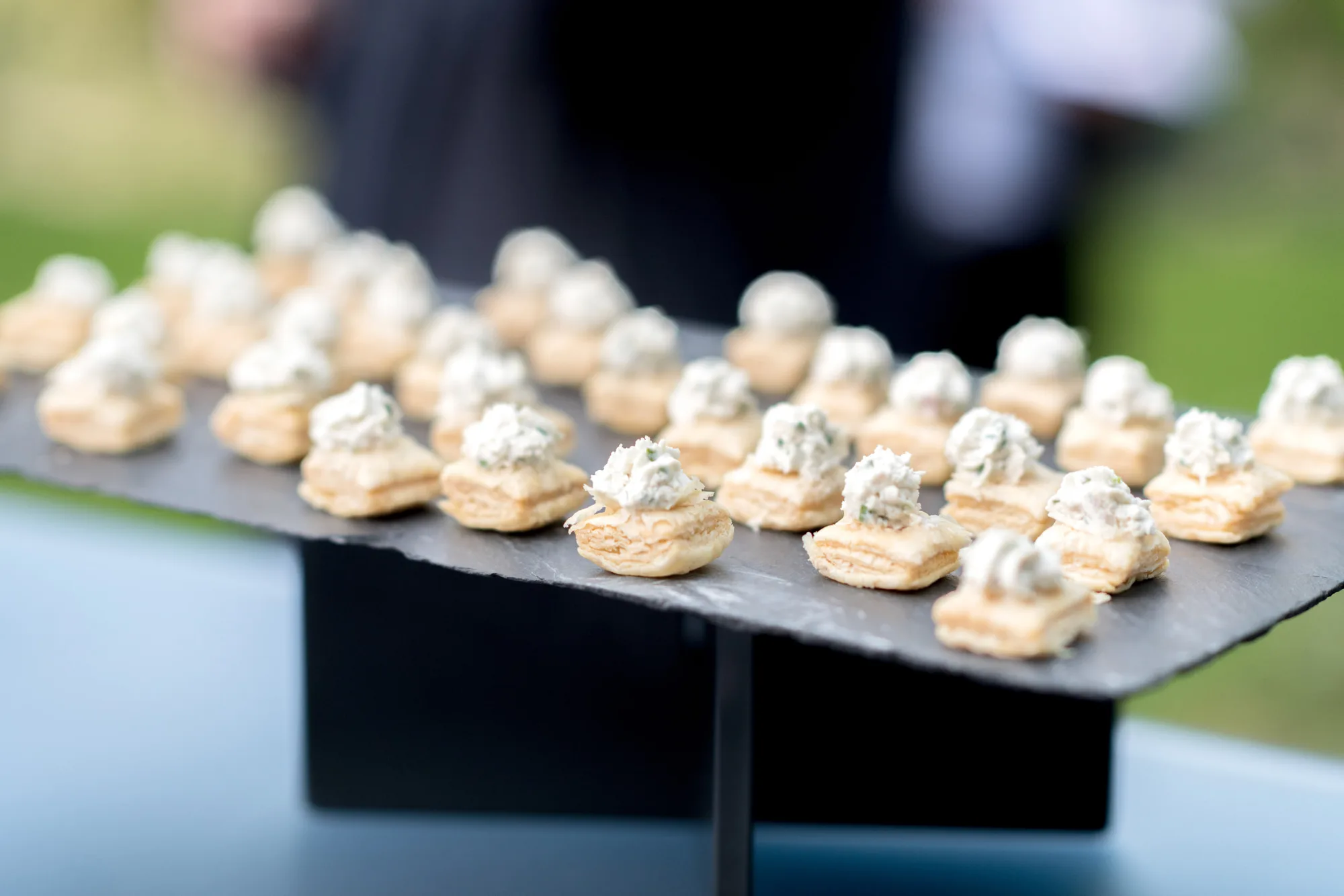 Mise en bouche feuilletée garnie de rillettes, dressée en rangs sur une ardoise lors d’un cocktail d’entreprise en extérieur