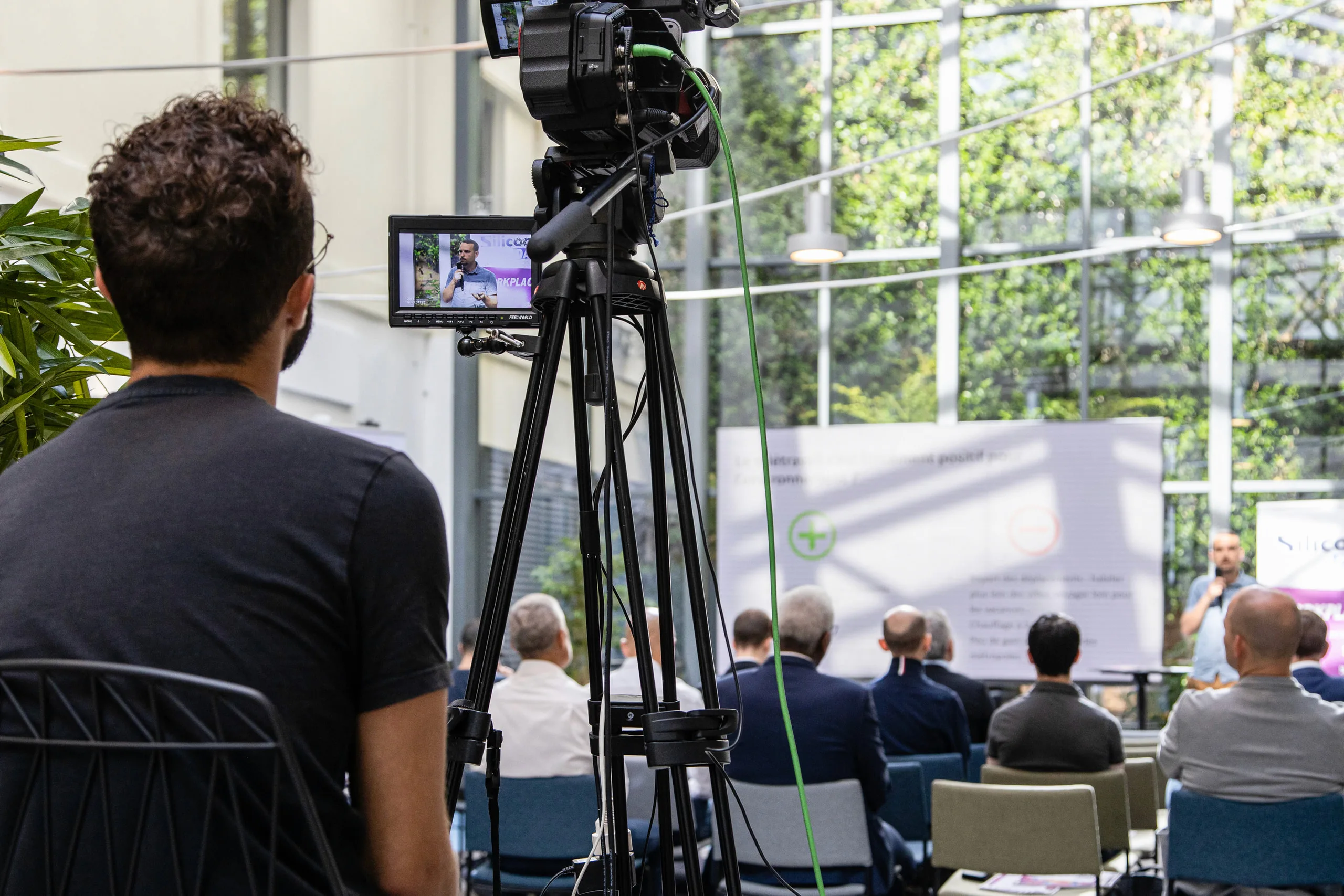 Captation vidéo d’une conférence : caméra sur trépied au premier plan, public de dos et intervenant au fond